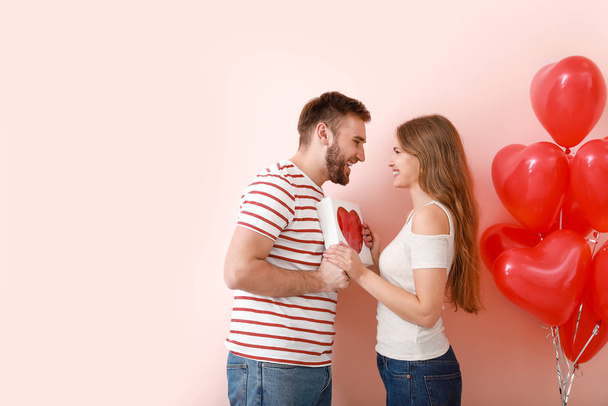 glückliches junges Paar mit Geschenk auf farbigem Hintergrund. Valentinstag-Feier - Foto, Bild