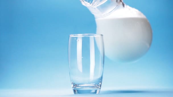 milk is poured into a glass on blue background - Πλάνα, βίντεο