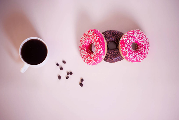 вкусные пончики с розовой глазурью и порошок с чашкой ароматного кофе на белом деревянном фоне
. - Фото, изображение