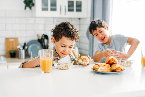 真の兄弟の間の2人の兄弟家庭で明るいキッチンで朝食を持っています。子供は食べたくない - 写真・画像