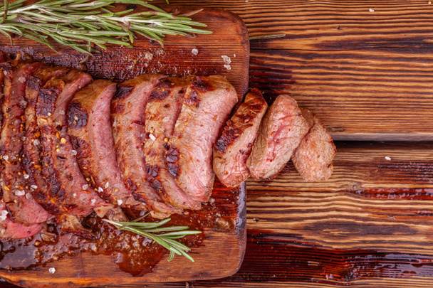 Krájený grilovaný hovězí steak Ribeye s kořením na rustikální dřevěné řezací desce - Fotografie, Obrázek