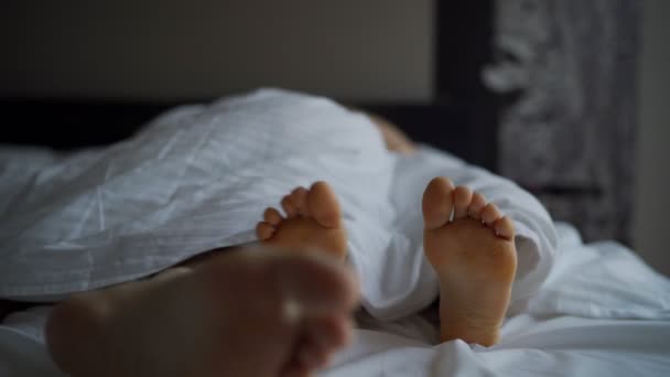 Shot of feet boyfriend and girlfriend lying in bed under blanket. - Imágenes, Vídeo