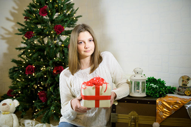 girl sits near a Christmas fir tree and holds in her hands a gift - Fotoğraf, Görsel