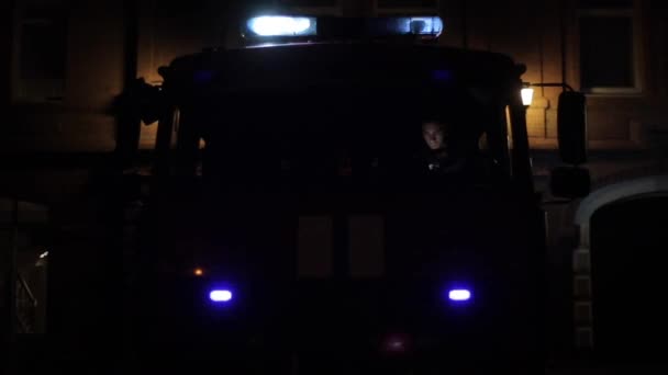 Przód wozu strażackiego z migającymi światłami awaryjnymi i syrenami w nocy. Strażak na przednim siedzeniu - Materiał filmowy, wideo