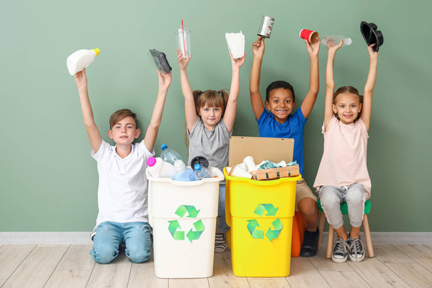 Crianças pequenas e recipientes com lixo perto da parede de cor. Conceito de reciclagem
 - Foto, Imagem