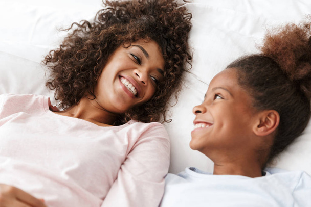 Image of cheerful african american woman and her daughter lying  - Фото, зображення