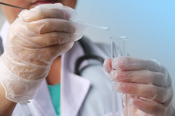 trabajador médico en guantes pone una muestra para el análisis de ADN en un hisopo de algodón en un tubo de ensayo de vidrio, el concepto de examen científico y médico, primer plano
 - Foto, Imagen