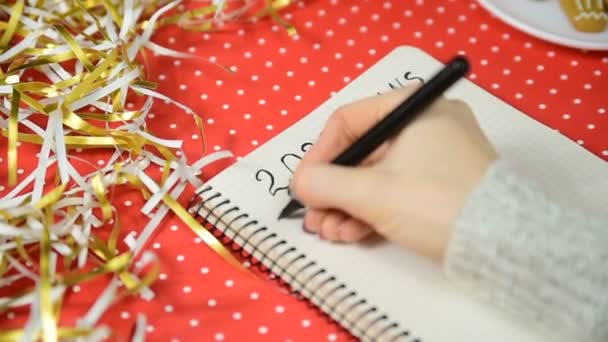 Kobiece ręce piszące plany na 2020 rok w notesie. Czerwone tło i świecidełko. Koncepcja noworoczna - Materiał filmowy, wideo