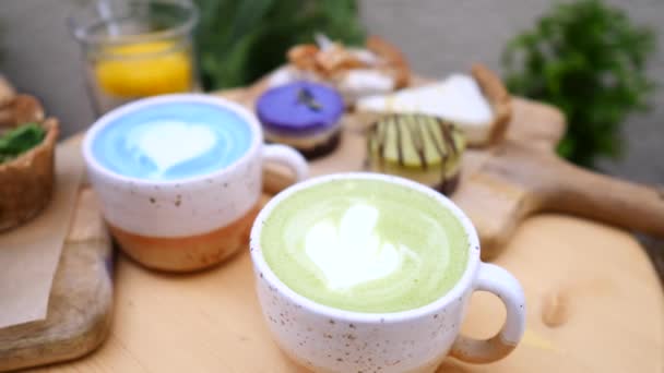 Matcha Zielona herbata Latte i Blue Matcha Latte w kubkach na stole. - Materiał filmowy, wideo