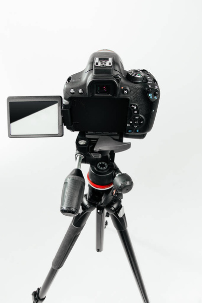 Photo camera with a tilting LCD screen on the tripod back view. Studio shot on white background - Photo, Image