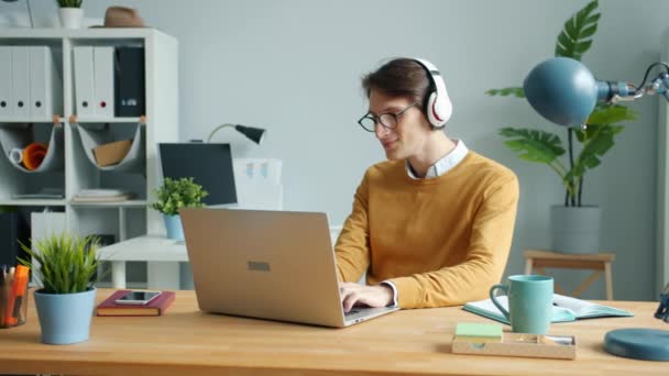 Handsome guy wearing headphones is listening to music in modern office at work - Filmmaterial, Video