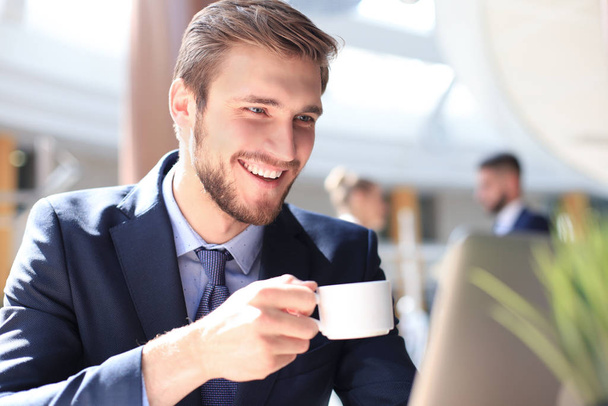 young businessman drinking coffee in office while typing on computer. - Foto, afbeelding