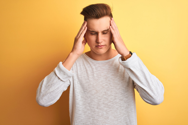 Young handsome man wearing white casual t-shirt standing over isolated yellow background with hand on head for pain in head because stress. Suffering migraine. - Photo, Image