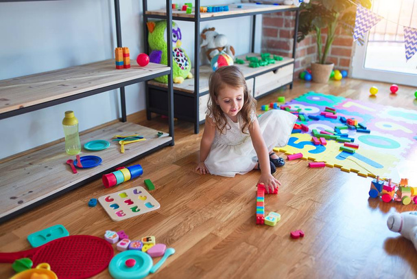 Imádnivaló szőke kisbaba játszik építőkockák körül sok játék óvodában - Fotó, kép
