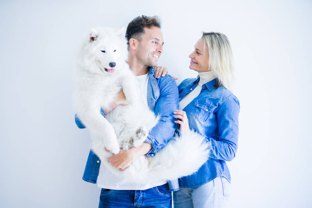Young beautiful couple holding dog standing over isolated white background - Foto, Bild