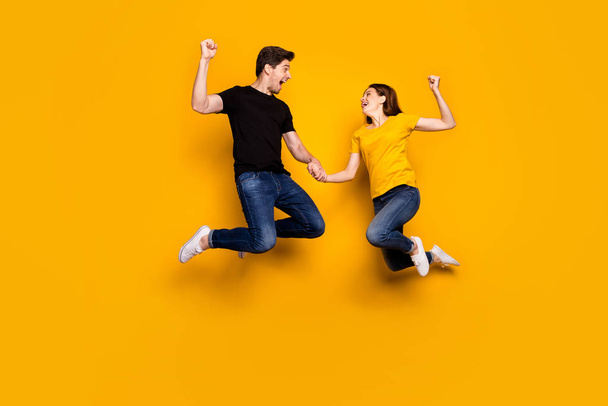 Full body photo of crazy guy lady couple jump high raise fists celebrate first place football league favorite team wear casual jeans t-shirts isolated yellow color background - Valokuva, kuva
