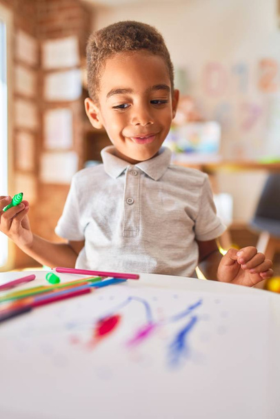 Прекрасний афроамериканець малює з паперу і маркер, які посміхаються в дитячому садку. - Фото, зображення