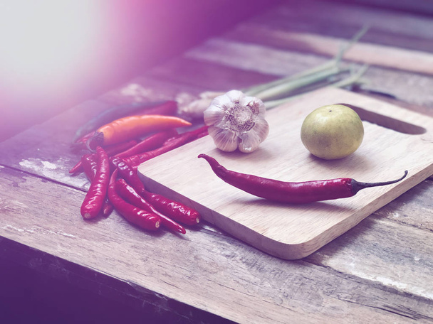 close up of chili peppers, garlic and lime on wooden cutting board - Фото, изображение
