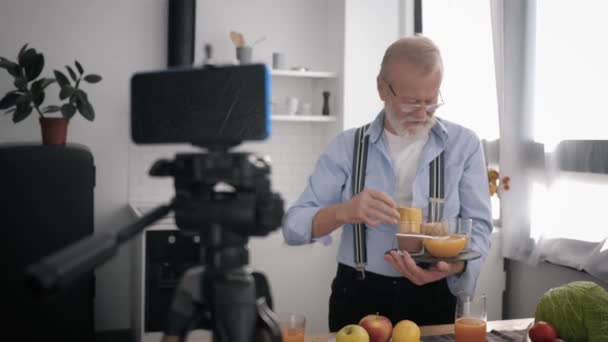 現代の高齢男性は台所を背景に携帯電話にvlogを書き健康的な食事を示すブログを保持します。 - 映像、動画