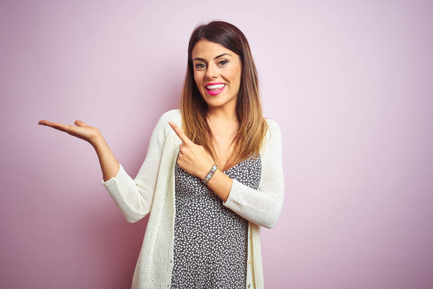 Young beautiful woman standing over pink isolated background amazed and smiling to the camera while presenting with hand and pointing with finger. - Photo, Image