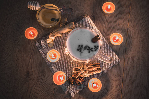 Скляна чашка традиційного індіанського чаю масала Чай освітлена свічками. Індійський чай масала Чай з молоком на сільському дерев "яному фоні, вибірковий фокус, копіювальний простір. Зачиніть..  - Фото, зображення