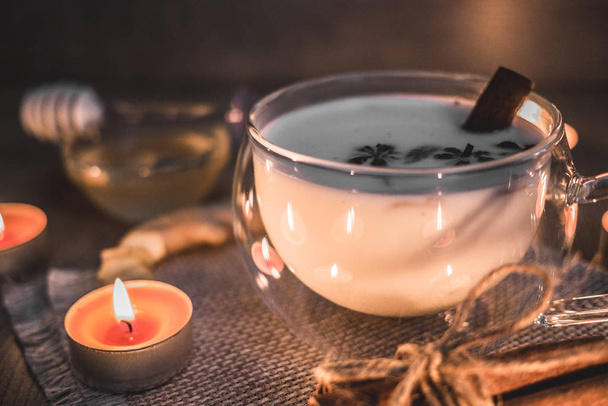 Ποτήρι φλιτζάνι παραδοσιακό ινδικό τσάι masala chai φωτίζεται από το φως των κεριών. Ινδικό τσάι masala chai - καρυκεύματα τσάι με γάλα σε ρουστίκ ξύλινο φόντο, επιλεκτική εστίαση, αντίγραφο χώρου. Κλείσε..  - Φωτογραφία, εικόνα