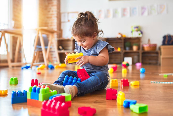 Beautiful toddler sitting on the floor playing with building blocks toys at kindergarten - Photo, Image