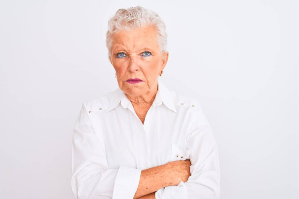 Starsza siwowłosa kobieta w eleganckiej koszuli stojąca nad odizolowanym białym tłem sceptyczna i nerwowa, dezaprobata wyraz twarzy z skrzyżowanymi ramionami. Osoba negatywna. - Zdjęcie, obraz