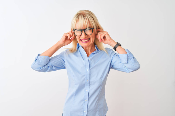 Podnikatelka středního věku v elegantní košili a brýlích na izolovaném bílém pozadí zakrývajícím uši prsty s otráveným výrazem pro hluk hlasité hudby. Hluchý koncept. - Fotografie, Obrázek