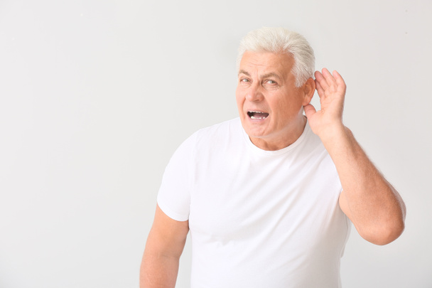 Hombre maduro con problemas de audición sobre fondo claro
 - Foto, imagen