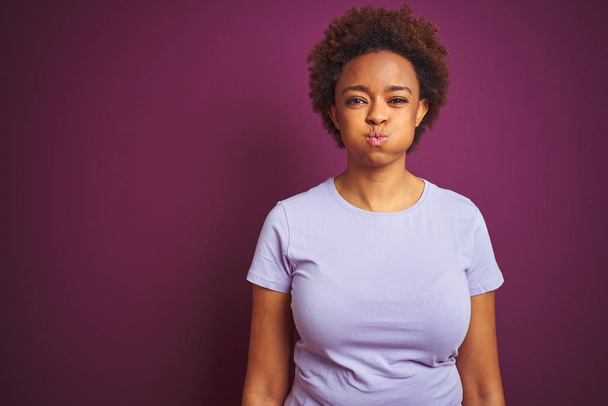 Young beautiful african american woman with afro hair over isolated purple background puffing cheeks with funny face. Mouth inflated with air, crazy expression. - Foto, Bild