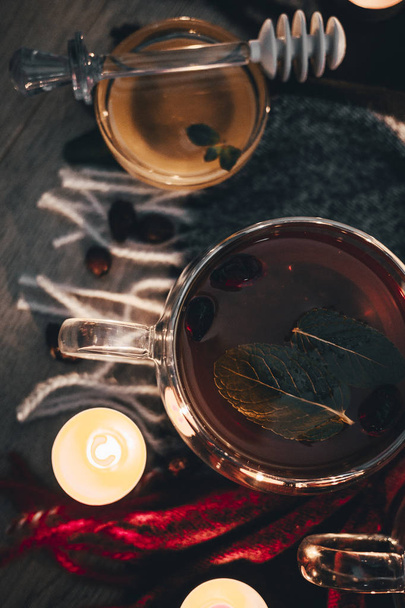 Black cup tea with dried rosehip and fresh leaves mint on the background of scattered dried rose hips and wax candles. Selective focus. Close up. Autumn and winter background.  - Foto, Imagem