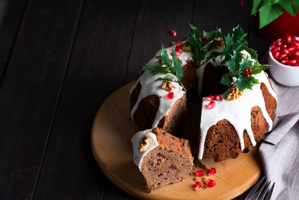Pastel de chocolate de Navidad con glaseado blanco y granos de granada sobre un fondo oscuro de madera con linterna roja y poinsettia
 - Foto, imagen