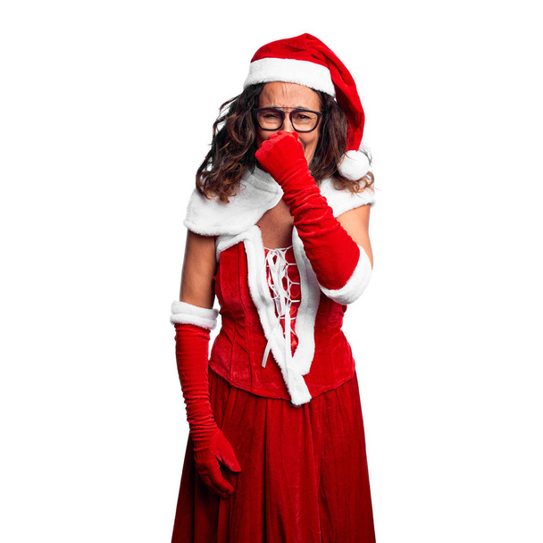 Mujer de mediana edad con traje de Santa Claus oliendo algo apestoso y asqueroso, olor intolerable, conteniendo la respiración con los dedos en la nariz. Concepto de malos olores
. - Foto, imagen