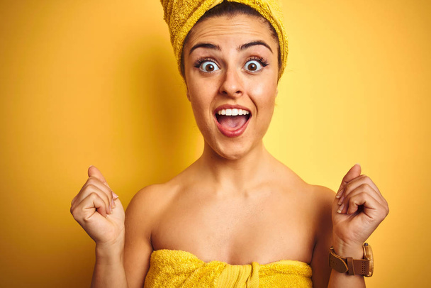 Молодая красивая женщина с полотенцем за душем на изолированном желтом фоне кричит гордо и празднует победу и успех очень взволнован, аплодисменты эмоции
 - Фото, изображение