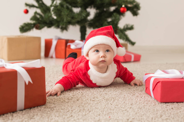 Linda niña con traje de Santa Claus arrastrándose por el suelo sobre el árbol de Navidad. Temporada de vacaciones
. - Foto, imagen