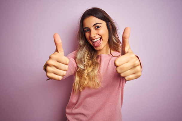 Молода красива жінка в светрі над рожевим ізольованим тлом, що схвалює позитивний жест рукою, великі пальці вгору посміхаються і щасливі для успіху. жест переможця
. - Фото, зображення