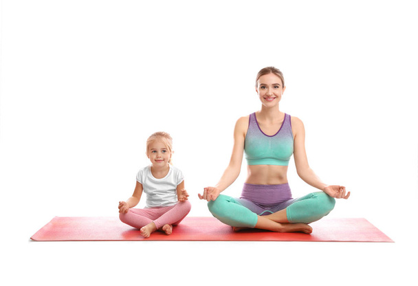 Young woman and her daughter doing exercise isolated on white. Home fitness - Fotó, kép