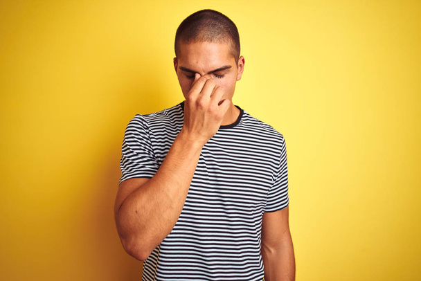 Młody przystojny mężczyzna w pasiastej koszulce na żółtym tle zmęczony pocieraniem nosa i oczu uczucie zmęczenia i ból głowy. Koncepcja stresu i frustracji. - Zdjęcie, obraz