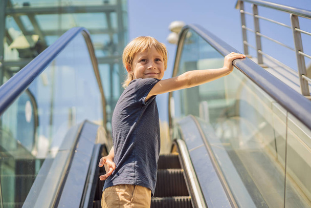 Μικρό αγόρι στις κυλιόμενες σκάλες στο εμπορικό κέντρο, υπαίθριο πορτρέτο - Φωτογραφία, εικόνα