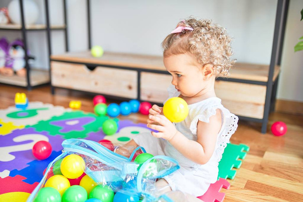Renkli oyun odasında beyaz güzel bir bebek oyuncaklarla oynuyor. Anaokulunda mutlu ve neşeli renkli balolar.. - Fotoğraf, Görsel