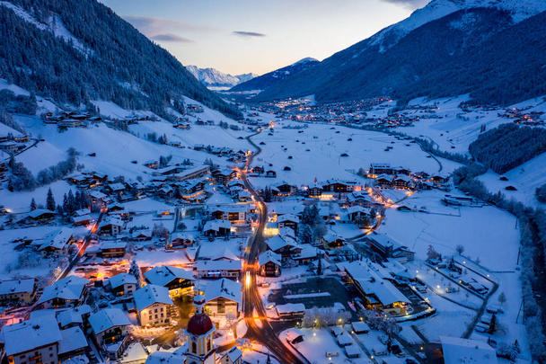 オーストリアの町ネウスティフトで冬の朝の街並み。町の中心部と教会の空中ビュー。住宅や交通信号の朝の照明。チロル、スツバイ渓谷 - 写真・画像