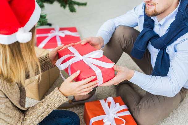 Christmas and holidays concept - Young happy couple wearing santa hats opening gifts at home. - Photo, Image