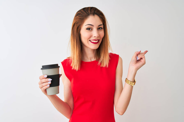 Nuori kaunis punapää nainen juo ottaa pois kahvia yli eristetty valkoinen tausta erittäin onnellinen osoittaa käsin ja sormella sivulle
 - Valokuva, kuva