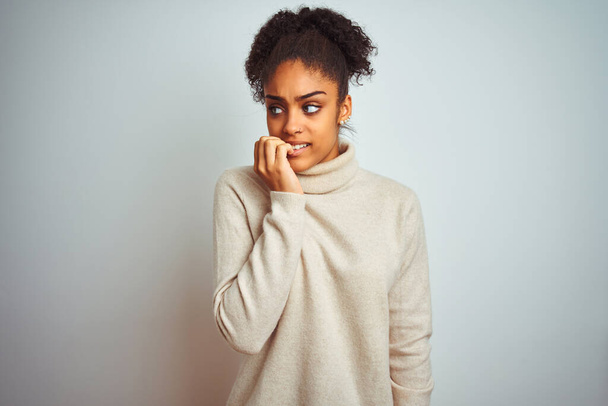 Mulher afro-americana vestindo camisola gola alta inverno sobre fundo branco isolado olhando estressado e nervoso com as mãos na boca mordendo unhas. Problema de ansiedade
. - Foto, Imagem