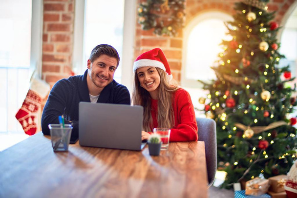 Young beautiful couple smiling happy and confident. Sitting on desk using laptop around christmas tree at home - Φωτογραφία, εικόνα