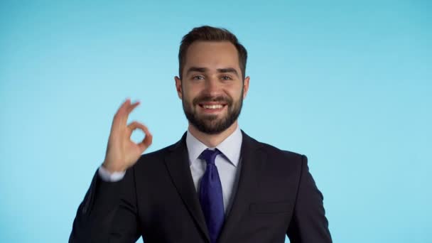 Positive businessman smiles to camera. Man showing OK sign over blue background - Кадри, відео