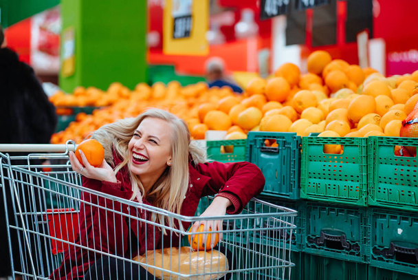 Pretty young hipster woman sitting in a supermarket trolley at the supermarket - 写真・画像