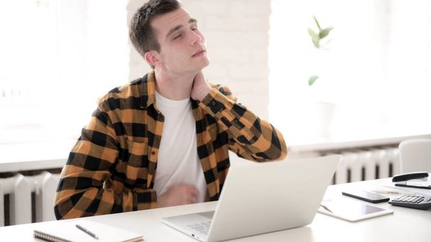 Випадковий молодий чоловік з болем у шиї працює на ноутбуці - Фото, зображення