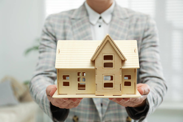 Real estate agent holding wooden house model indoors, closeup - Foto, Imagem
